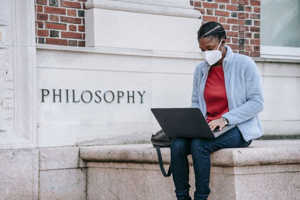 Young black female student using a laptop near a university building